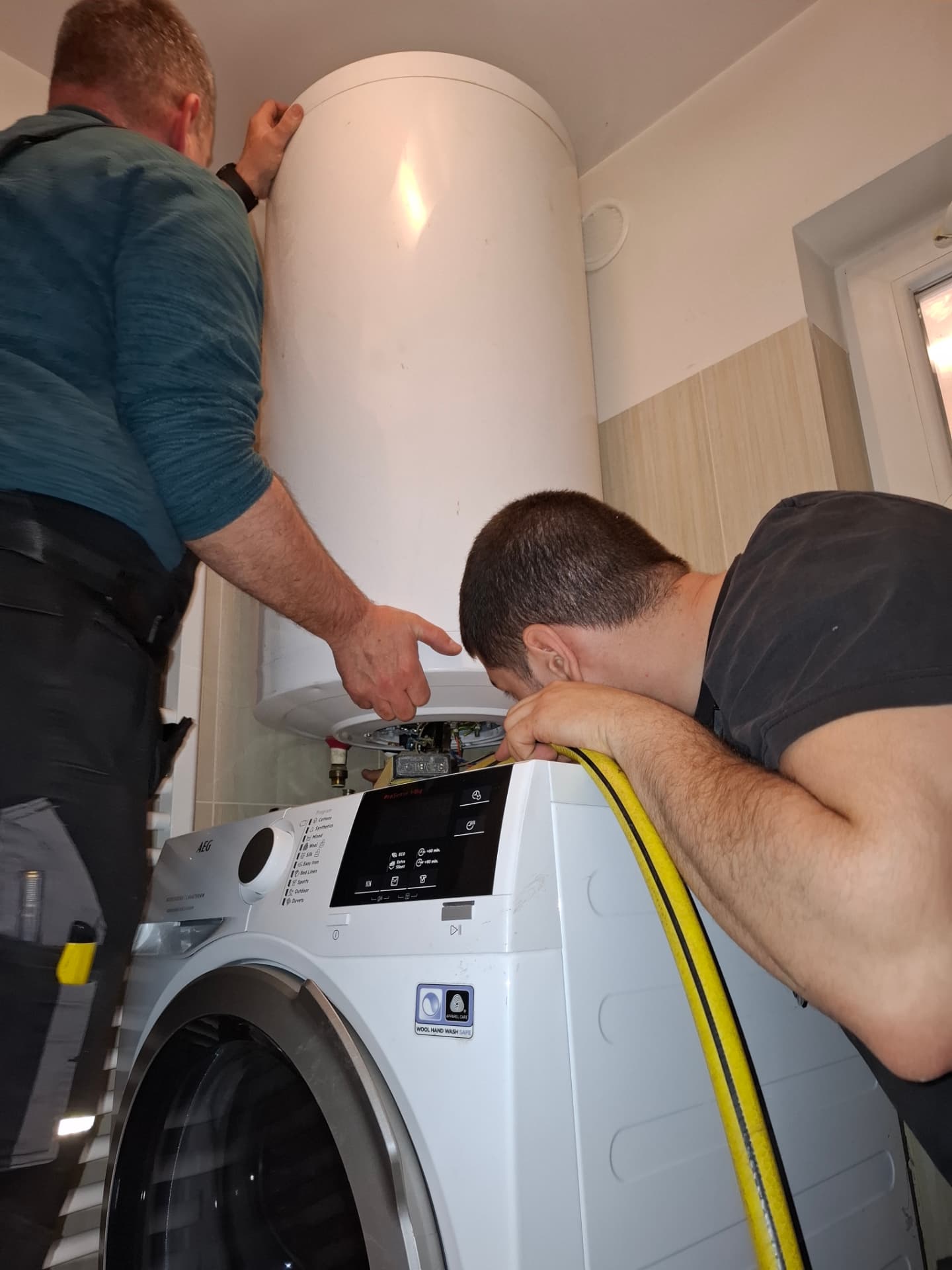 Két szerelő villanybojler szerelésén dolgozik egy budapesti fürdőszobában